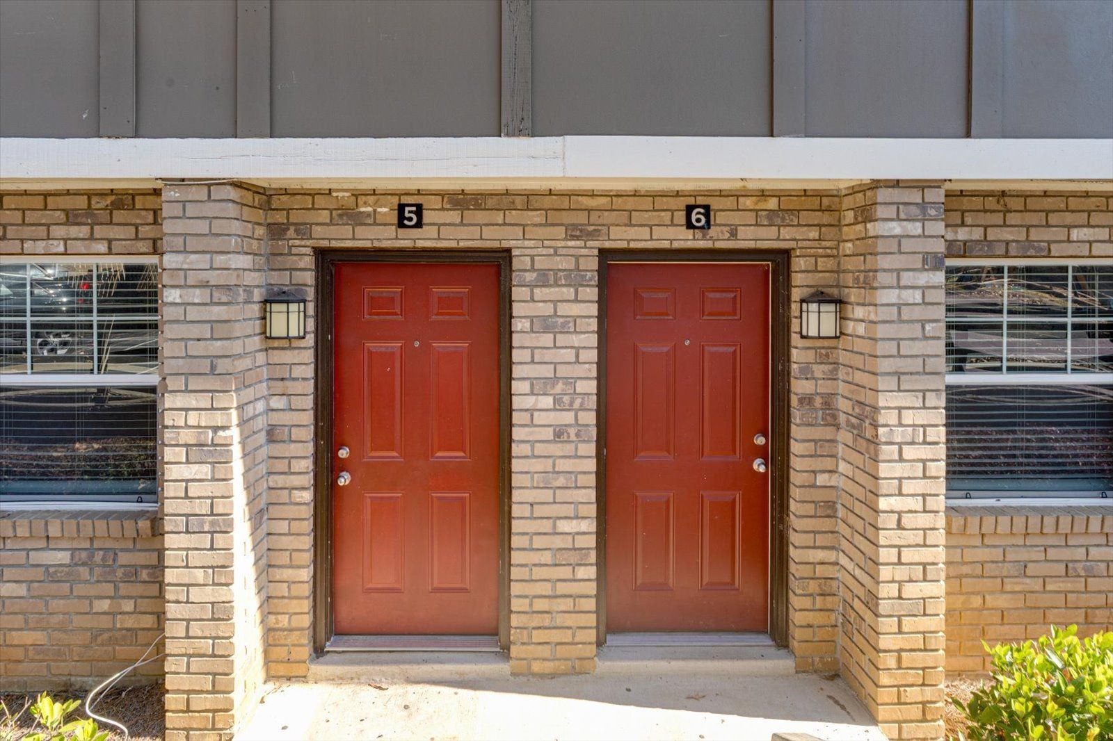 Two red apartment doors in a brick building entrance with windows on both sides