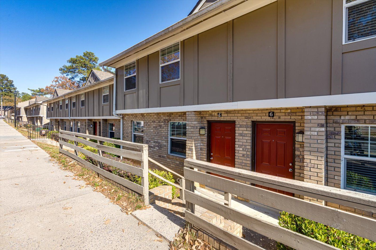 Row of tan apartment townhomes with red doors and white rail fence along a paved walkway