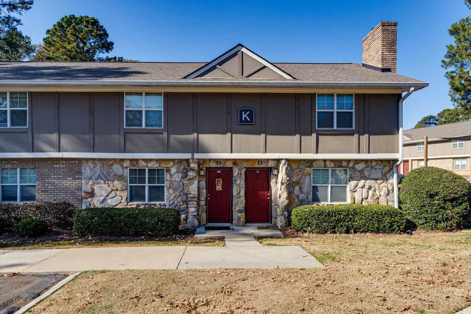 Two-story apartment building with red double doors, beige siding, and a small front lawn
