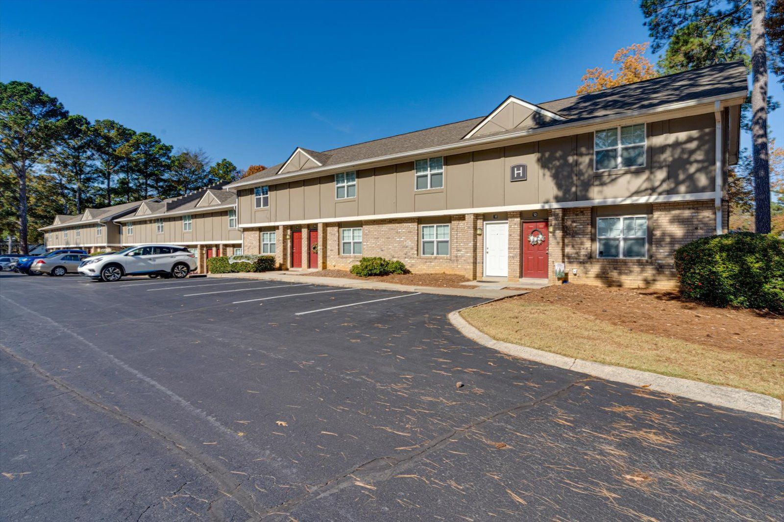 Apartment complex parking lot with tan two-story buildings and red doors under a blue sky