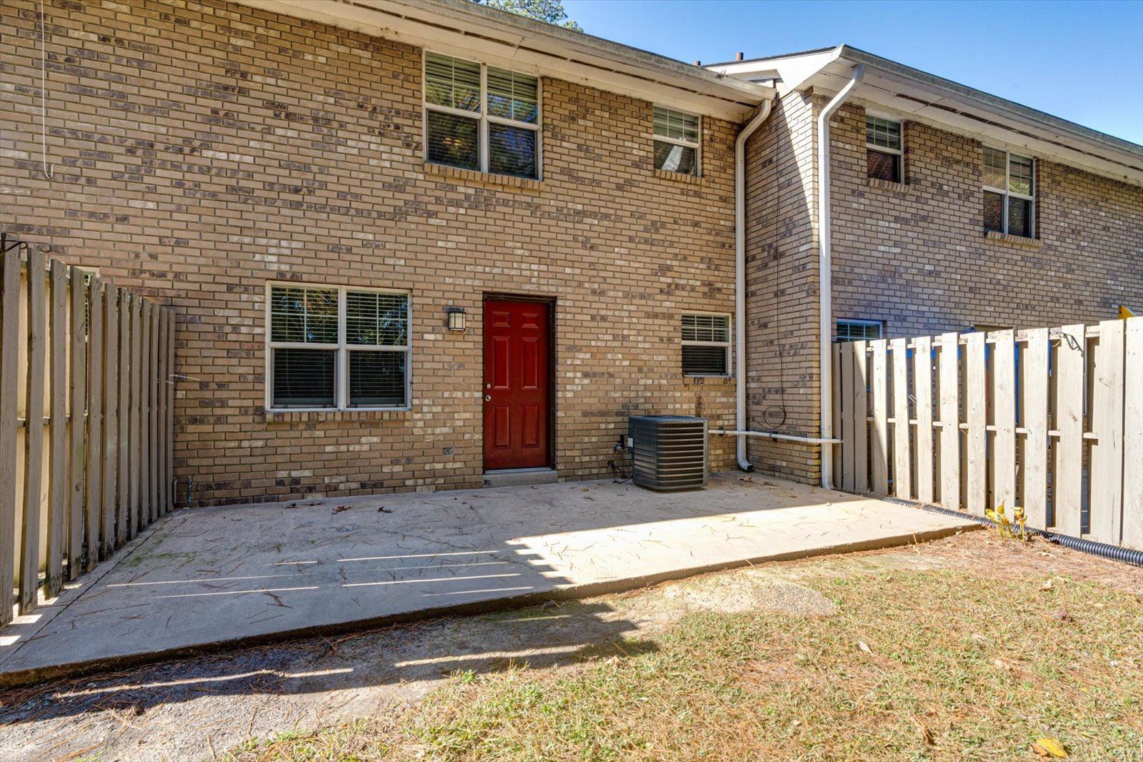 Brick townhouse patio with a red door, white fence, and small concrete yard