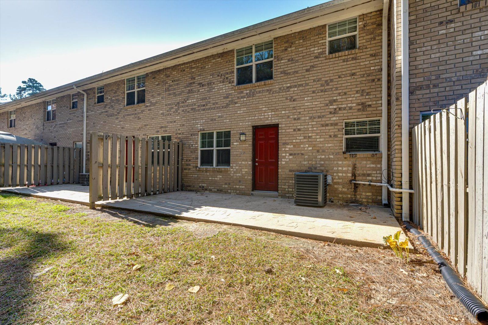 Backyard patio beside a brick townhouse with a red door and wooden fence
