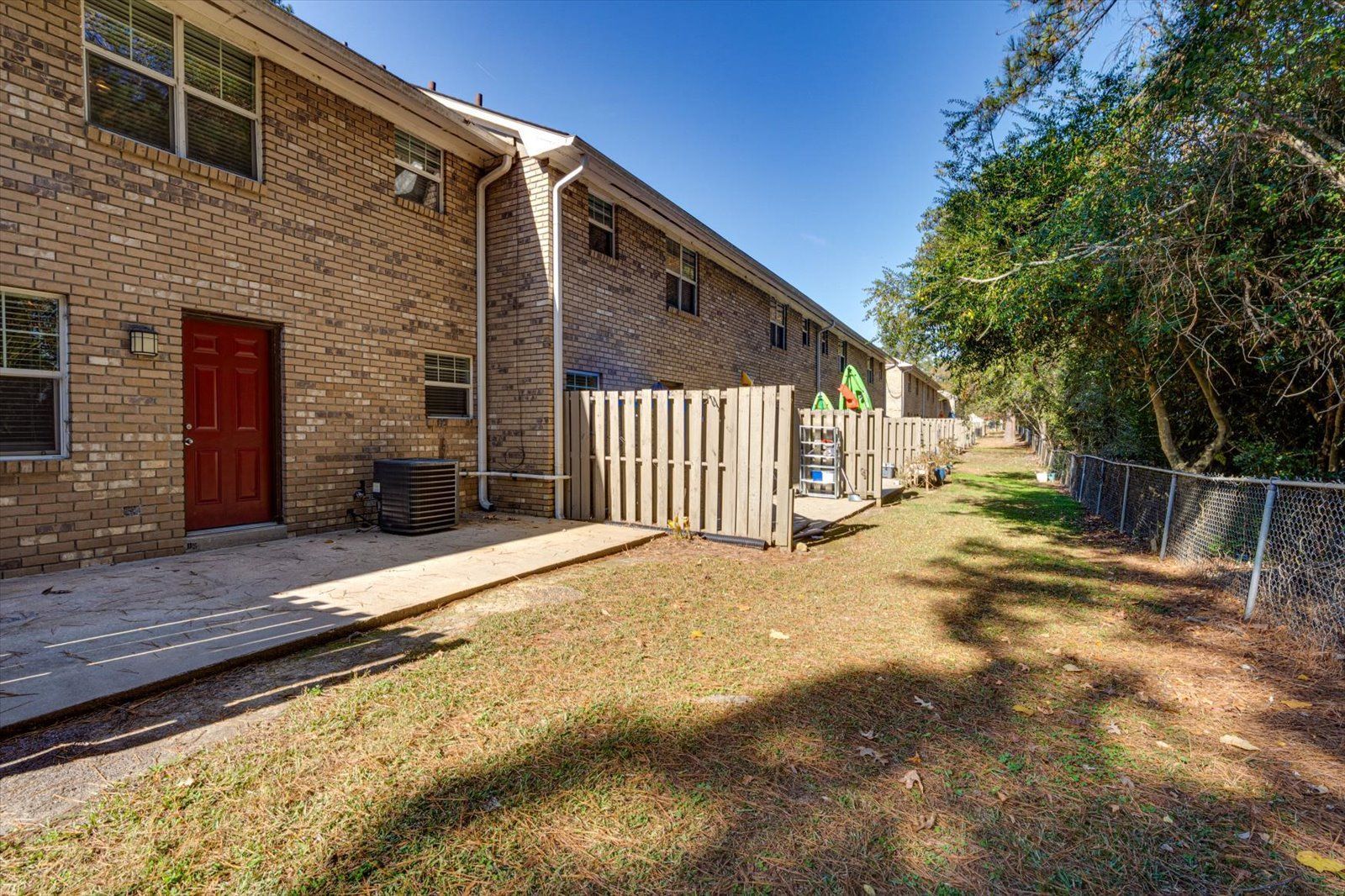 Brick apartment buildings with red doors beside a grassy yard and fence under clear blue sky