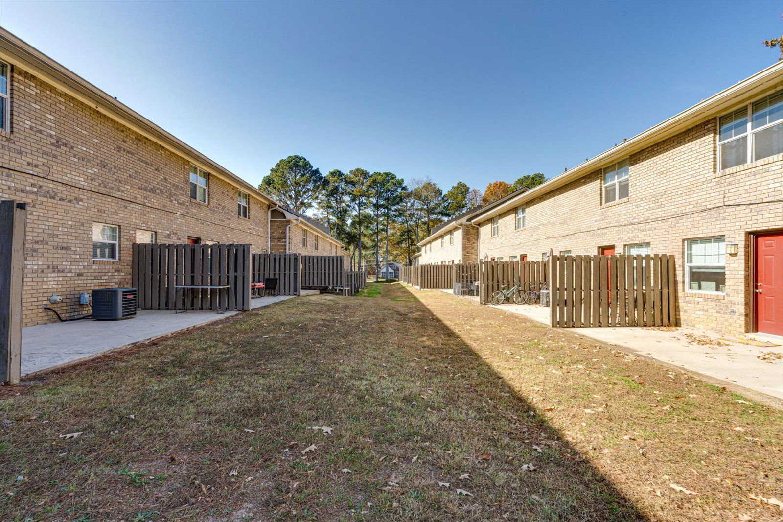 Apartment courtyard between brick buildings with fenced patios and a grassy center walkway.