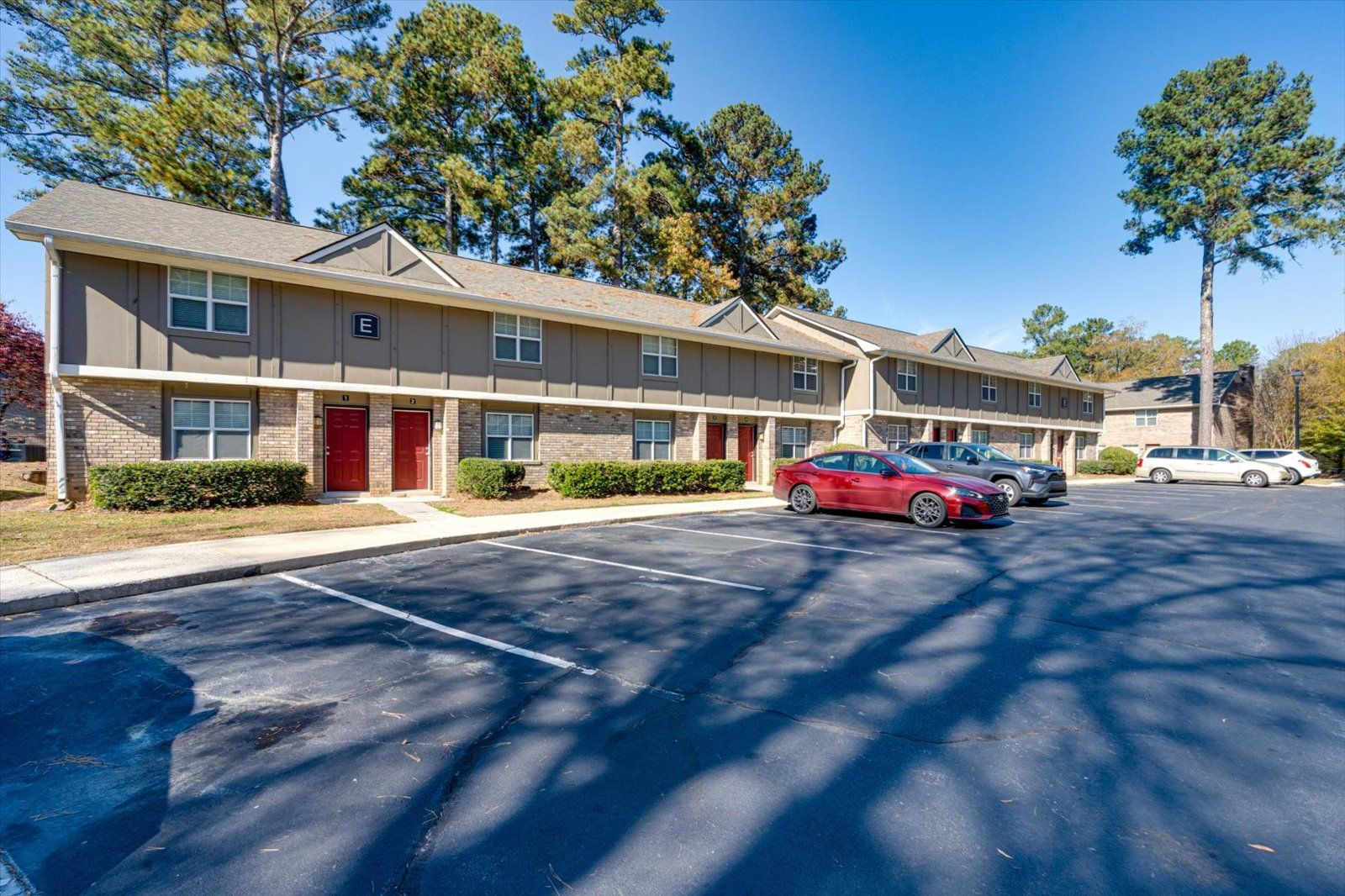 Two-story apartment complex with red doors and parked cars in front under a clear blue sky