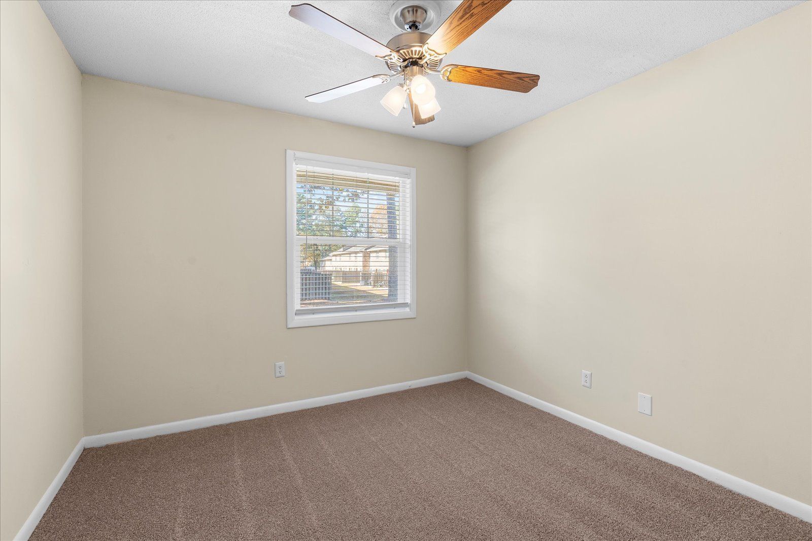Empty beige bedroom with carpet, a window, and a ceiling fan.