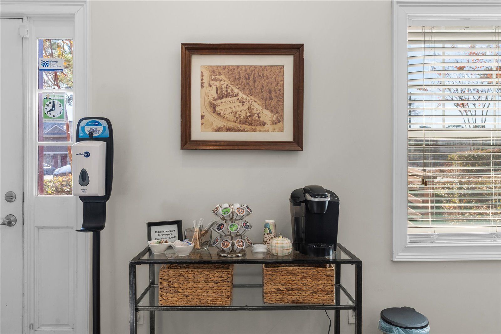 Home wall with framed art above a small console table, phone stand, wicker baskets, and a window.