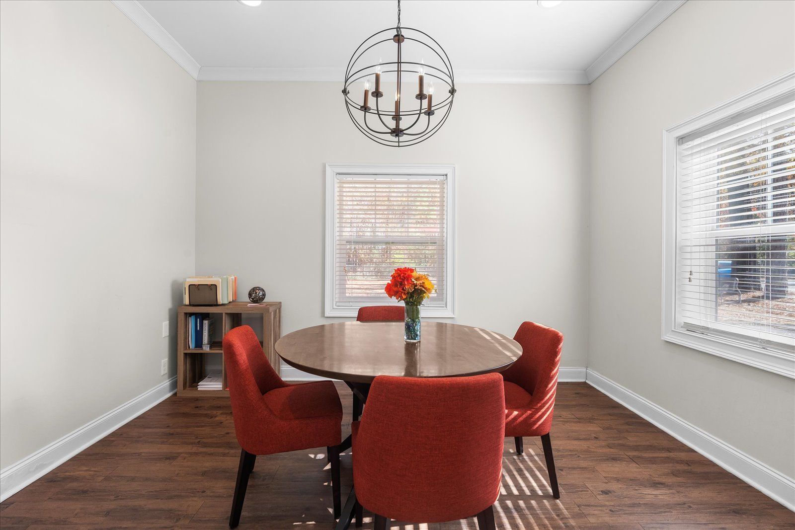 Dining room with round table, red chairs, white walls, and a hanging chandelier.