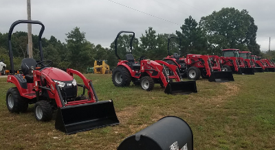 Red tractors lined up in a grassy field under cloudy skies, with a black mailbox in the foreground