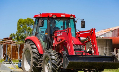 Red tractor with front loader parked on a farmyard under a blue sky