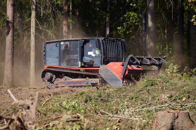 Forestry mulcher clearing brush in a forest; dust and debris rising.