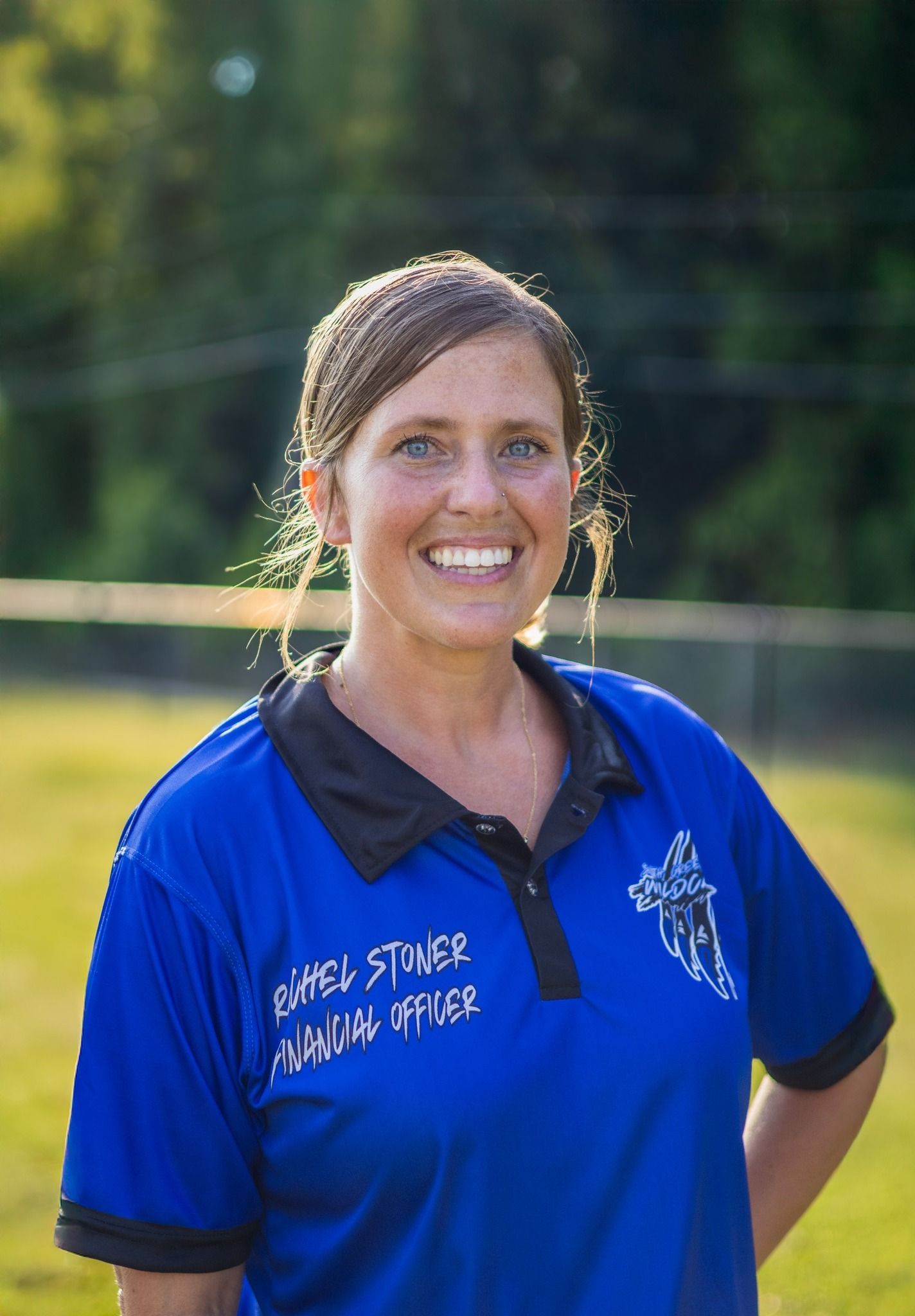 Man in green polo stands on a football field, arms crossed, stadium in background.