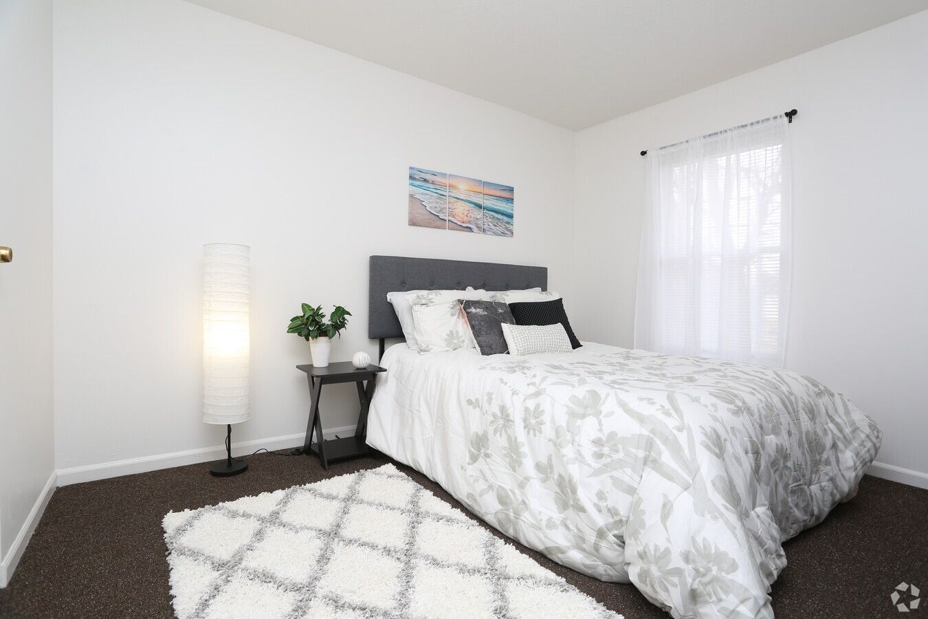 A bedroom with a bed , nightstand , lamp and rug.