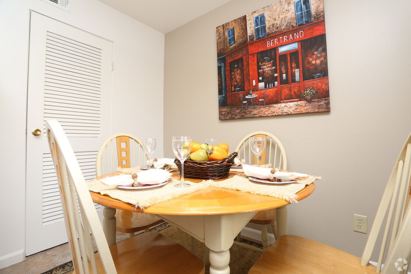 A dining room with a table and chairs and a painting on the wall.