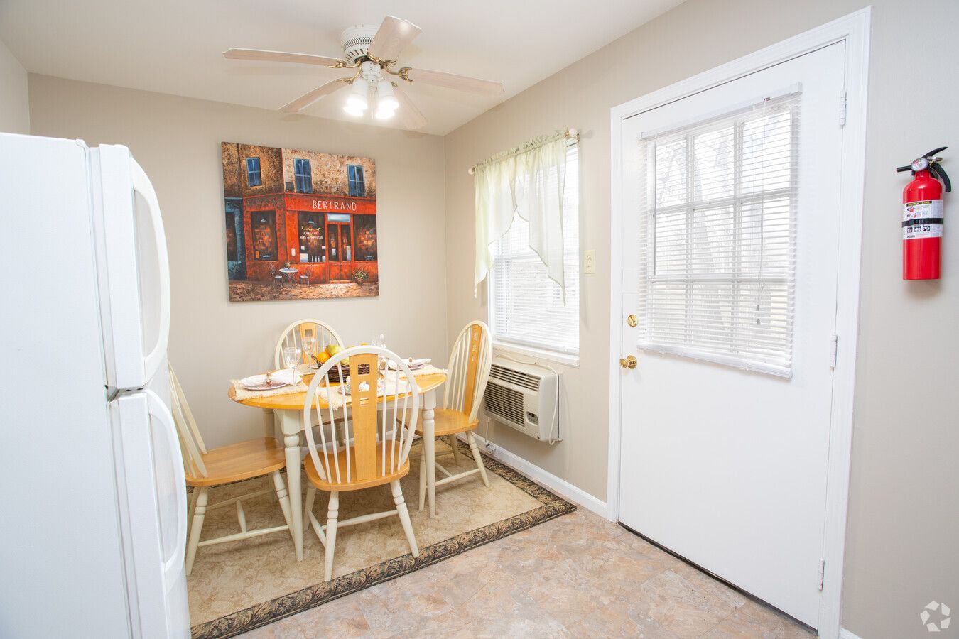 A dining room with a table and chairs , a refrigerator , and a fire extinguisher.