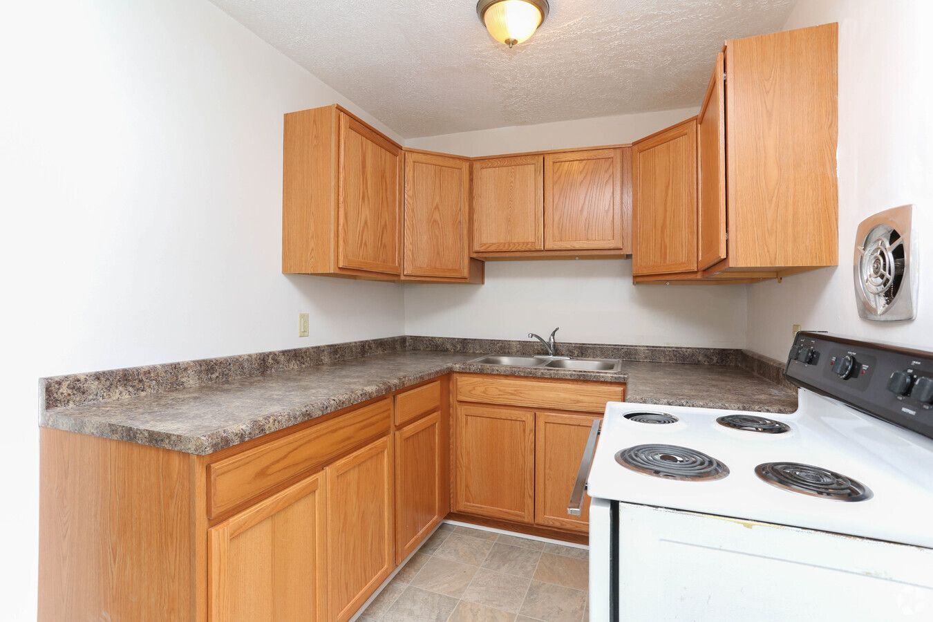 A kitchen with wooden cabinets , a white stove and a sink.