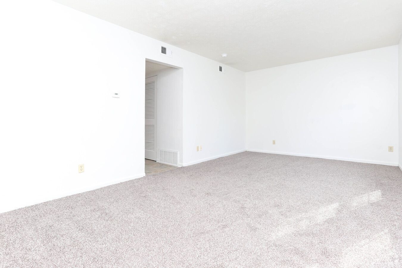 An empty living room with a carpeted floor and white walls.