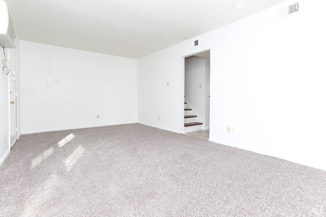 An empty living room with a carpeted floor and white walls.