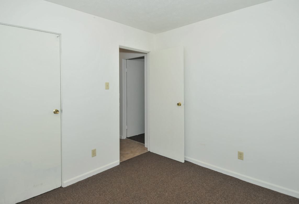 An empty bedroom with white walls and brown carpet