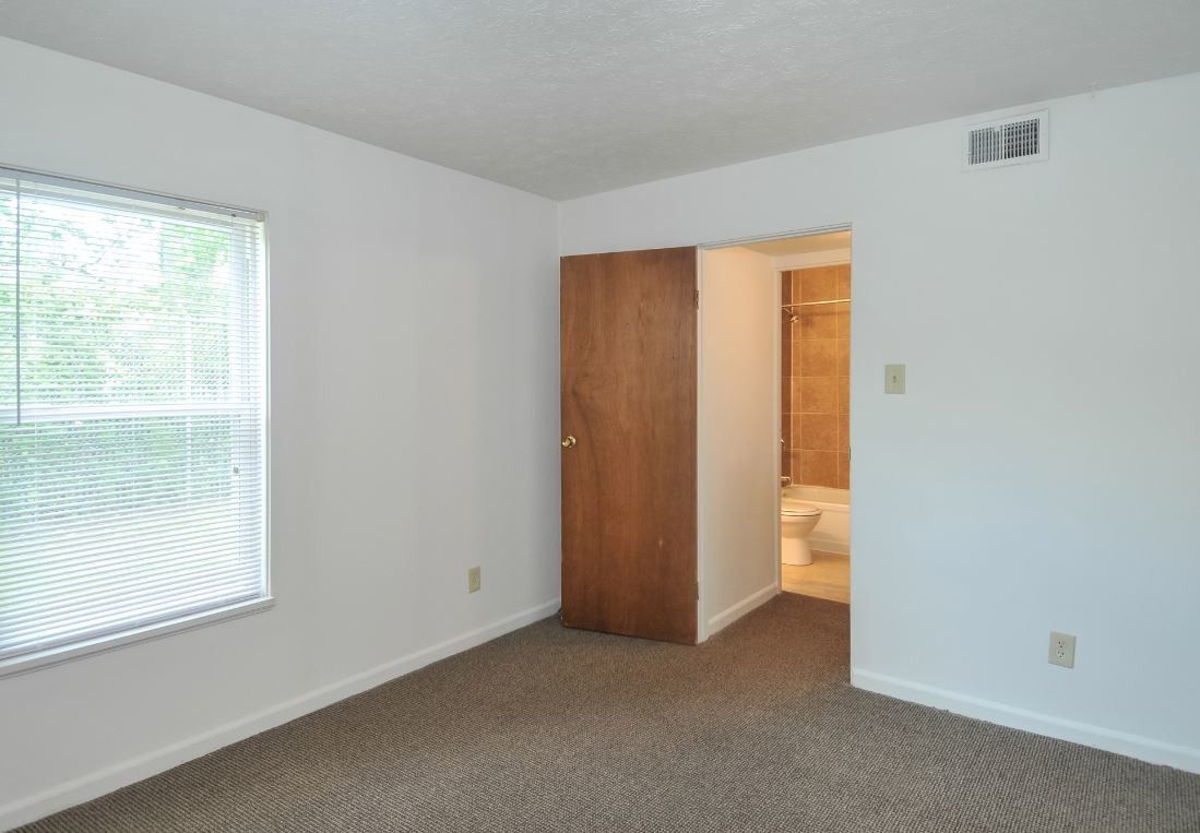 An empty bedroom with a window and a door leading to a bathroom.