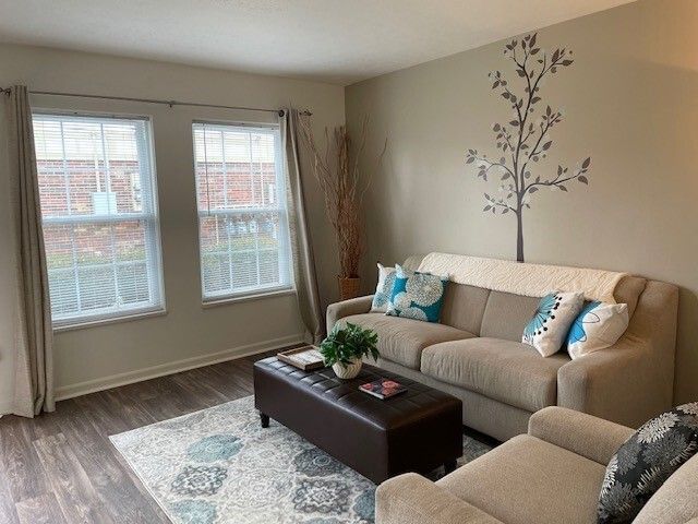 A living room with a couch , chair , coffee table and two windows.