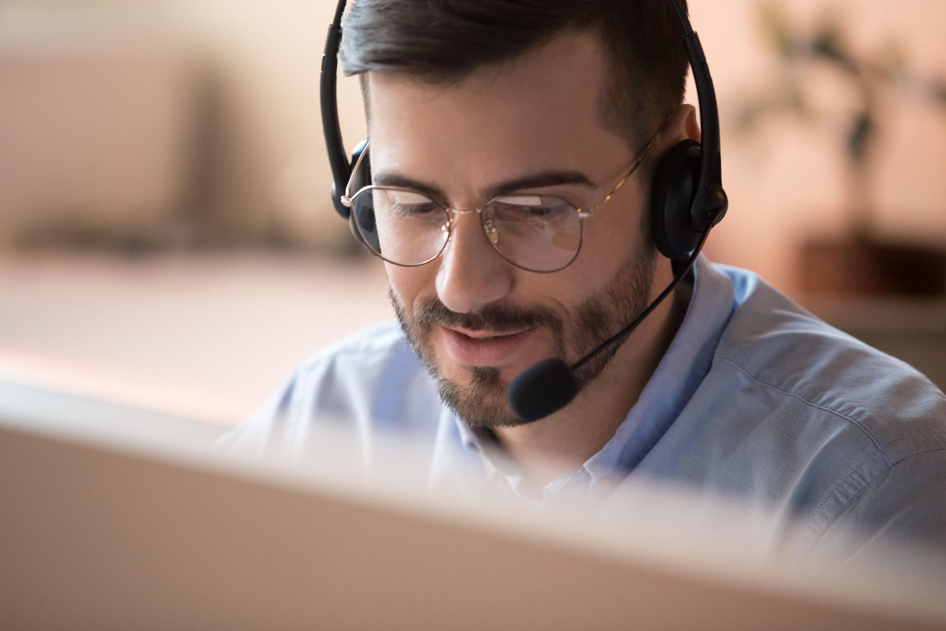 A man wearing headphones and glasses is sitting in front of a computer.