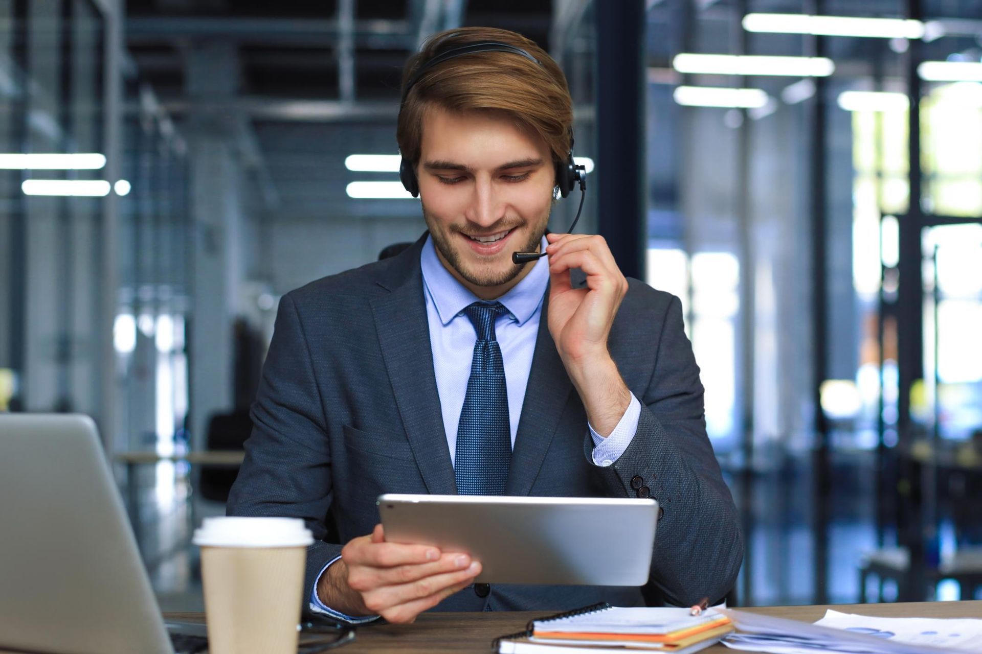 A man wearing a headset is sitting at a desk using a tablet computer.
