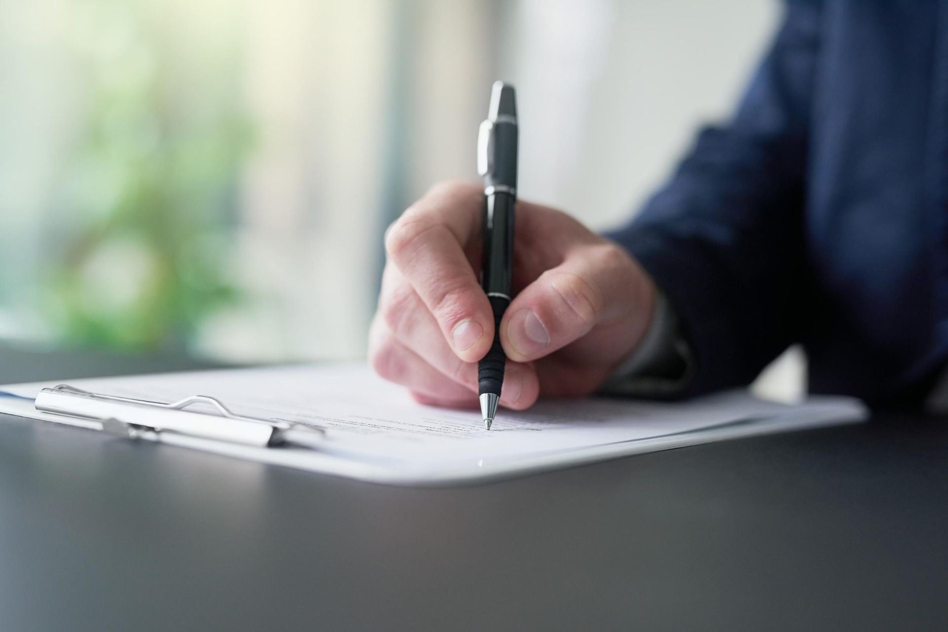 A man is writing on a piece of paper with a pen.