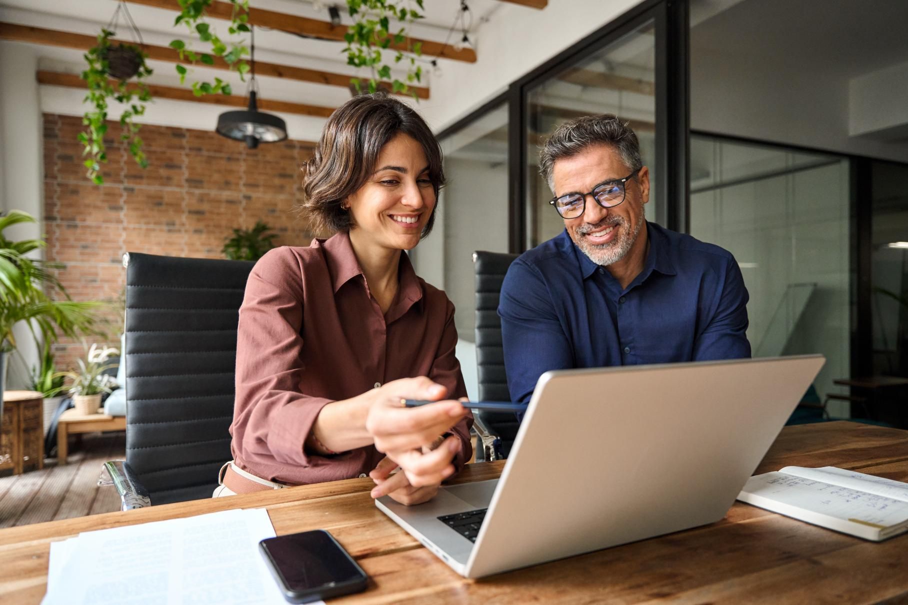 A man and a woman are sitting at a table looking at a laptop computer.