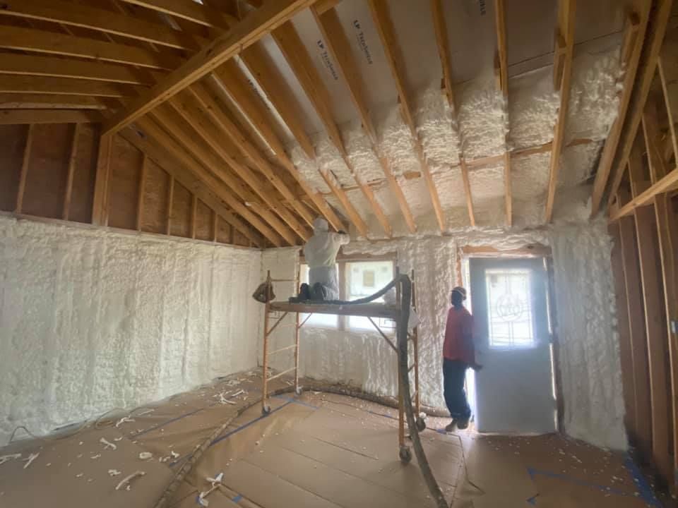 Interior of a building under construction, walls and ceiling being insulated with white foam.