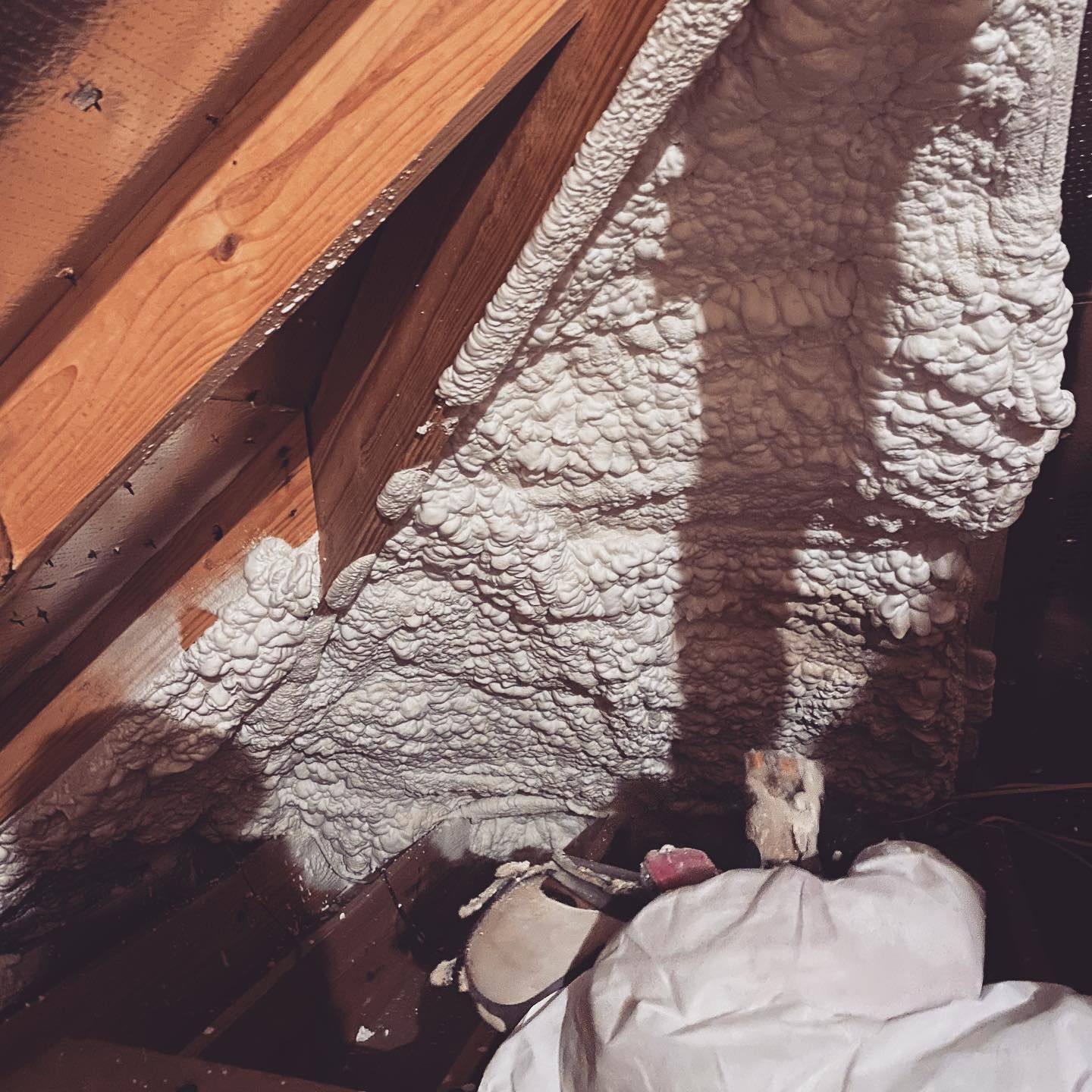 Foam insulation sprayed between wooden rafters in an attic. White foam fills the space.