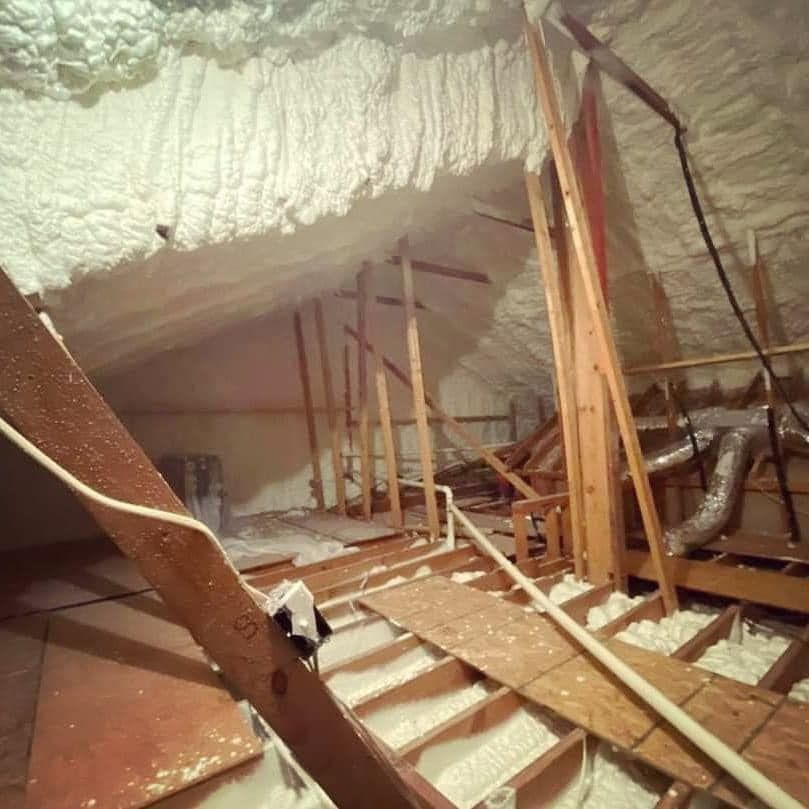 Attic interior with spray foam insulation. Wooden rafters and beams are visible.