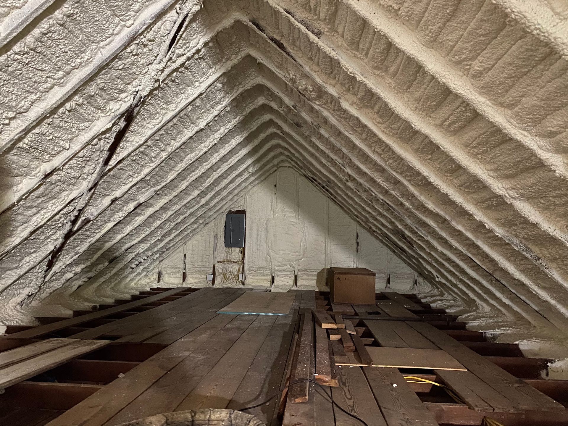 Attic with spray foam insulation on roof and walls, wood floor with various objects.