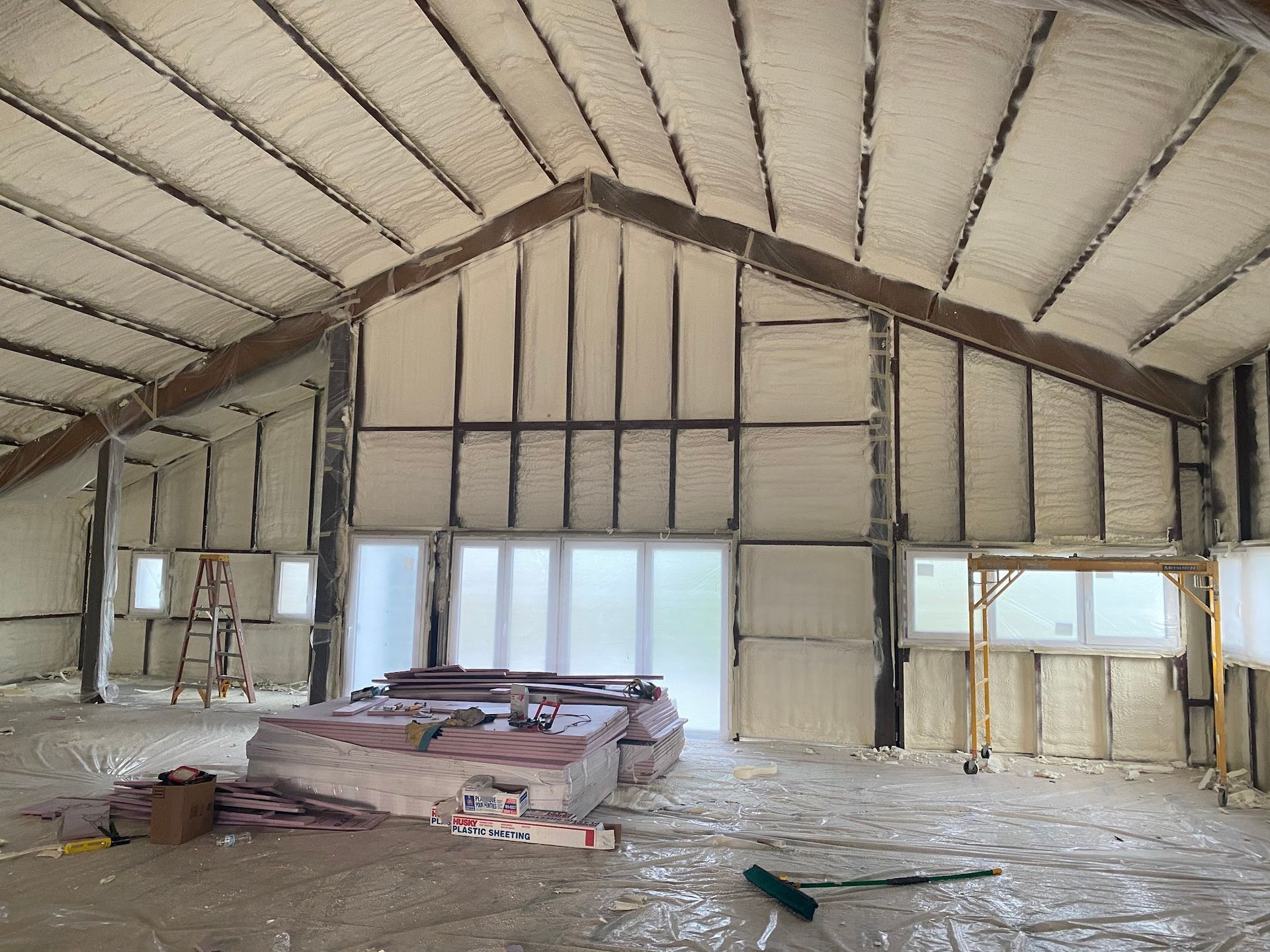 Interior of a building with spray foam insulation on the walls and ceiling, construction materials on the floor.
