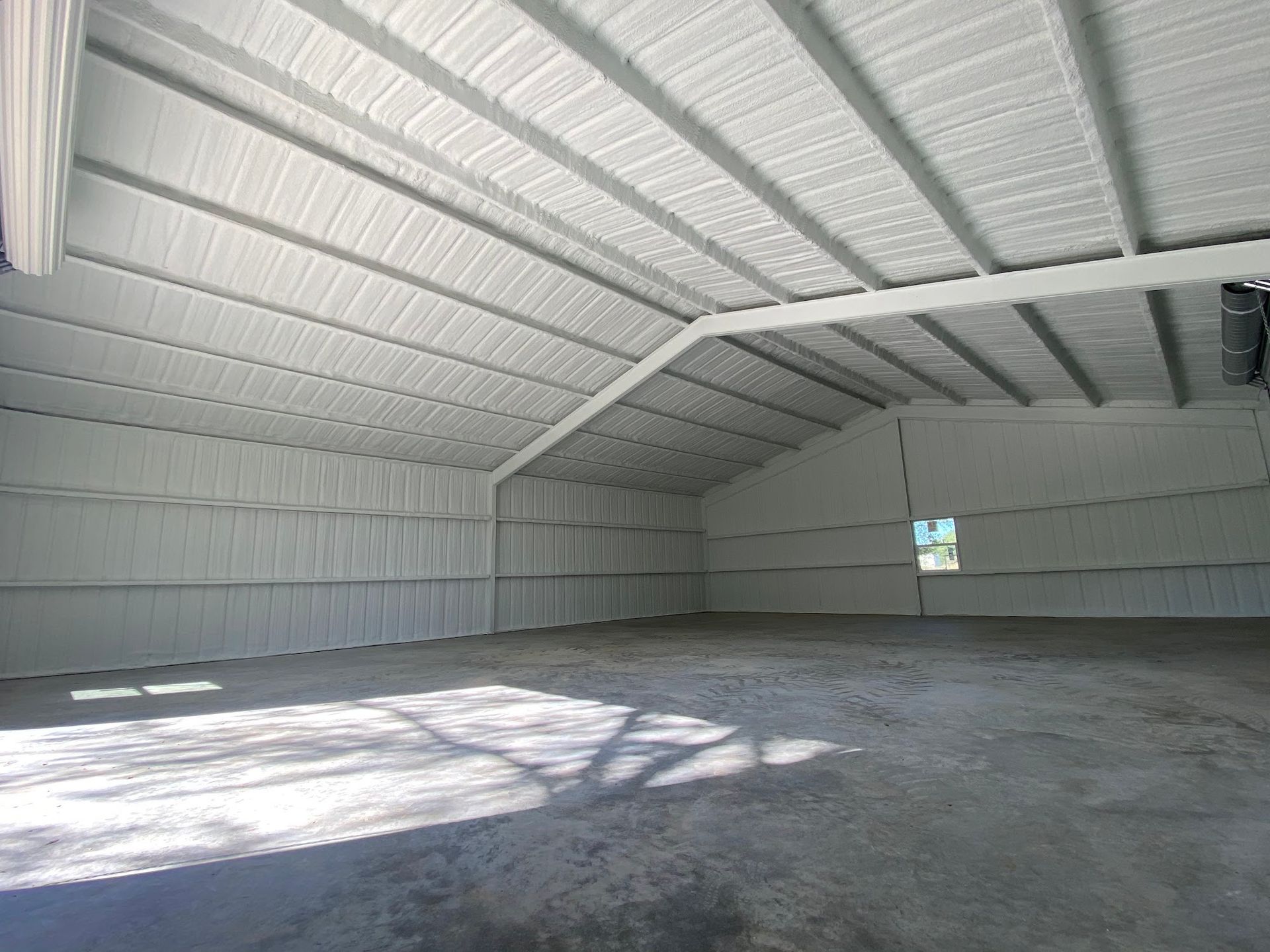 Interior view of a white metal building with a concrete floor and a high, pitched roof.