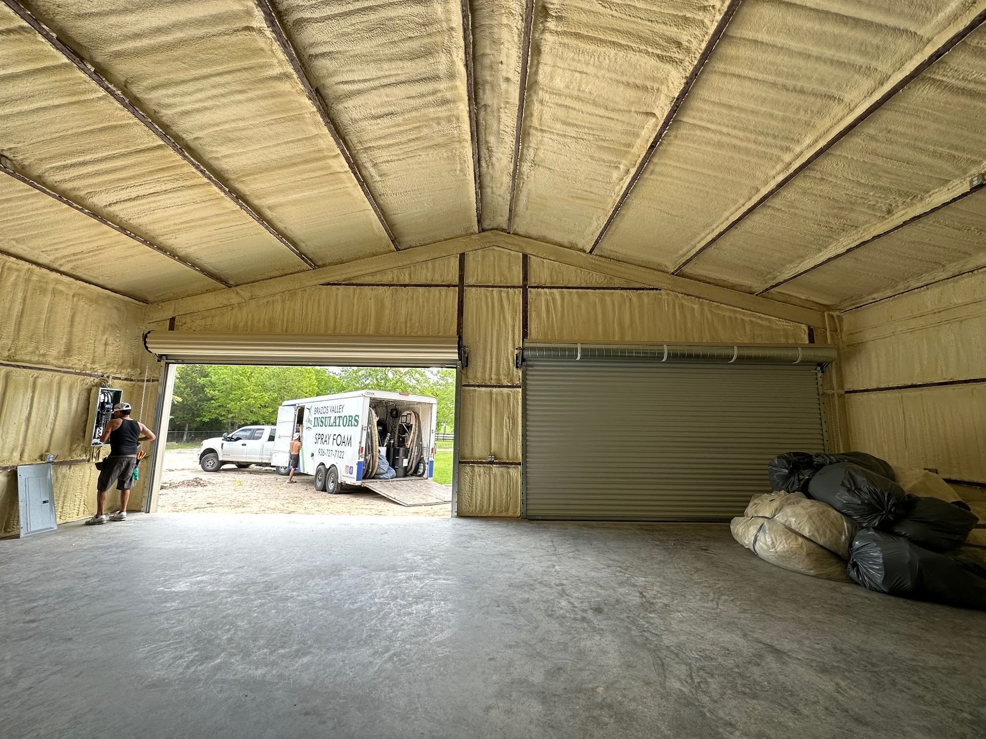 Interior of a metal building with spray foam insulation. A truck is parked outside the open door.