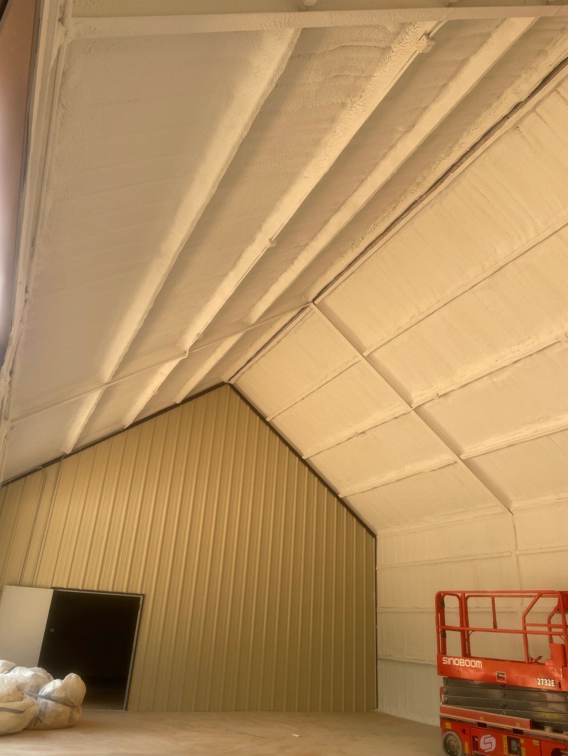 Interior view of a building with spray foam insulation on the roof and walls; a lift is visible.