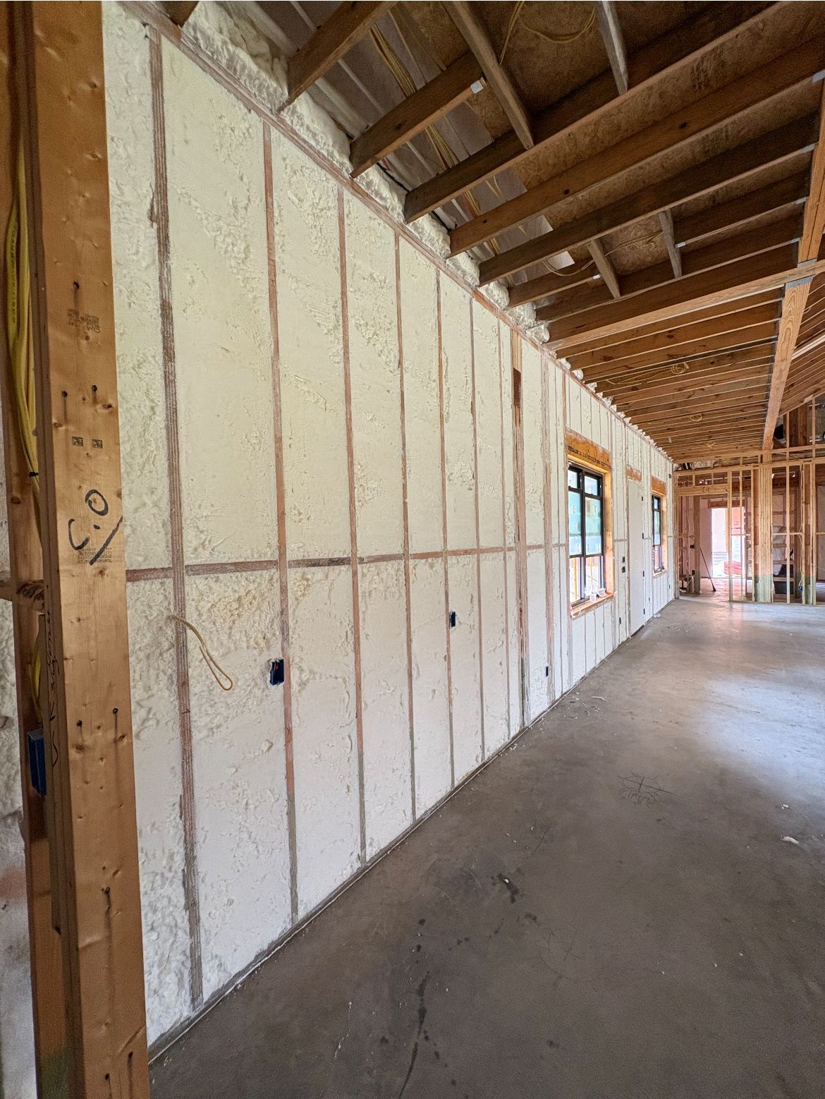 Interior of a building under construction. Insulation between wooden beams, window frames visible, concrete floor.