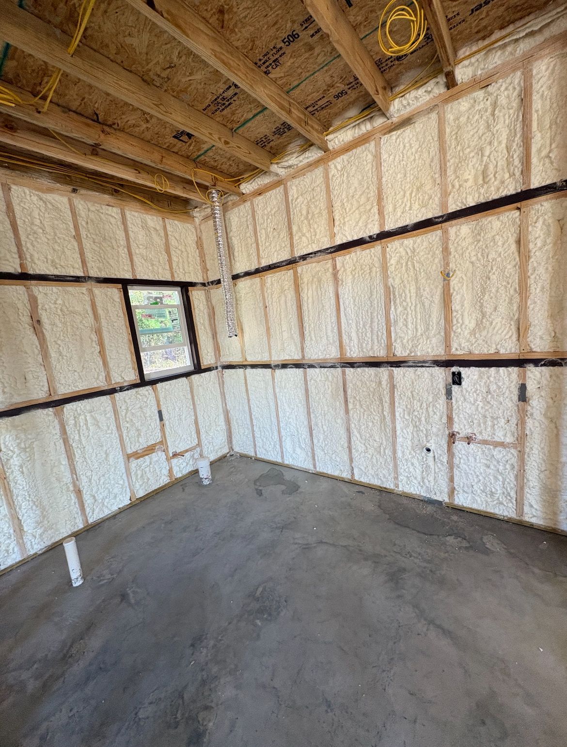 Interior of a building under construction, spray foam insulation on walls, concrete floor, small window.