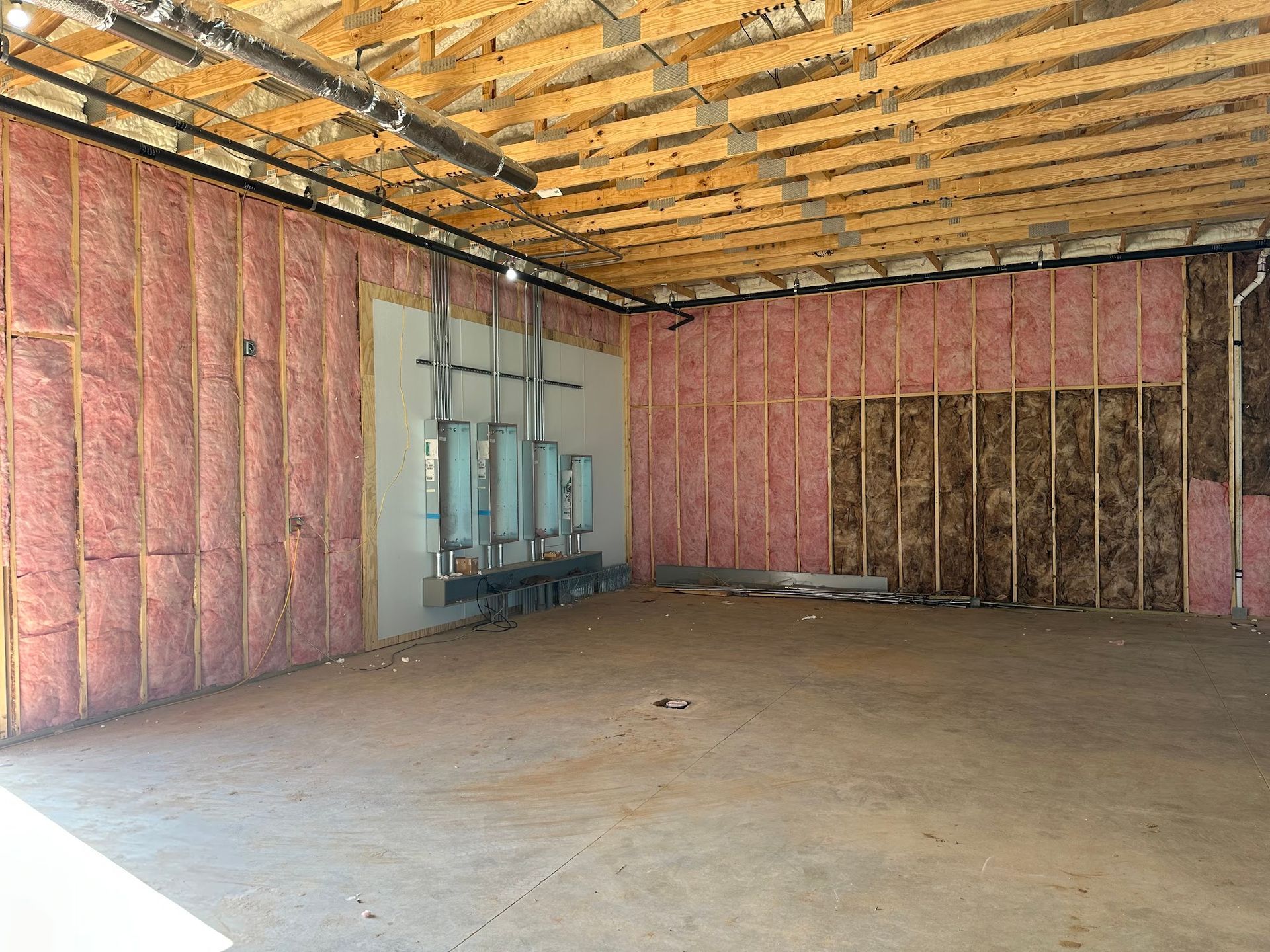 Interior of a building under construction. Pink insulation lines the walls. The ceiling has exposed wooden beams.