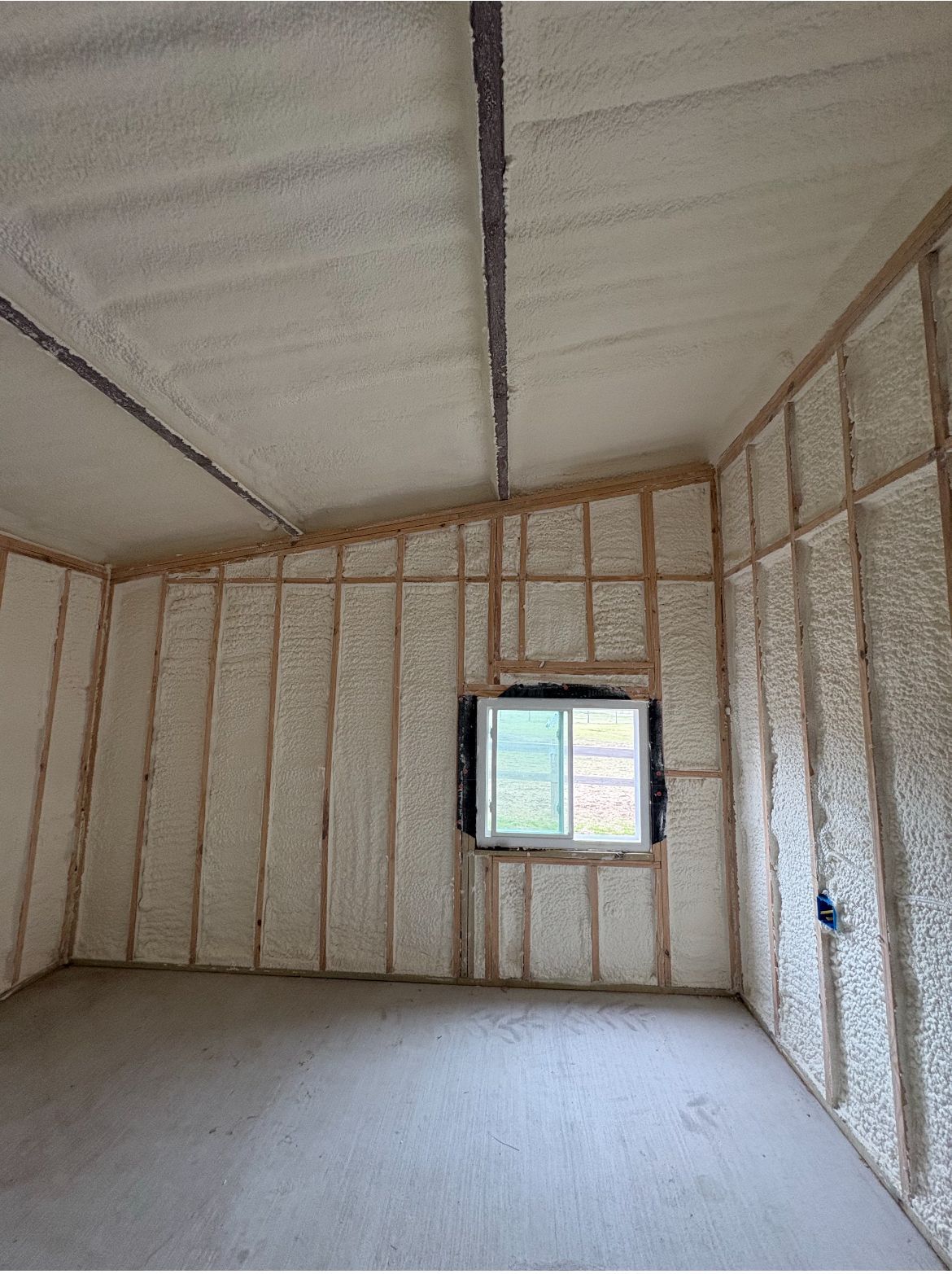 Interior of a room with spray foam insulation on walls and ceiling. A window is in the center of the wall.