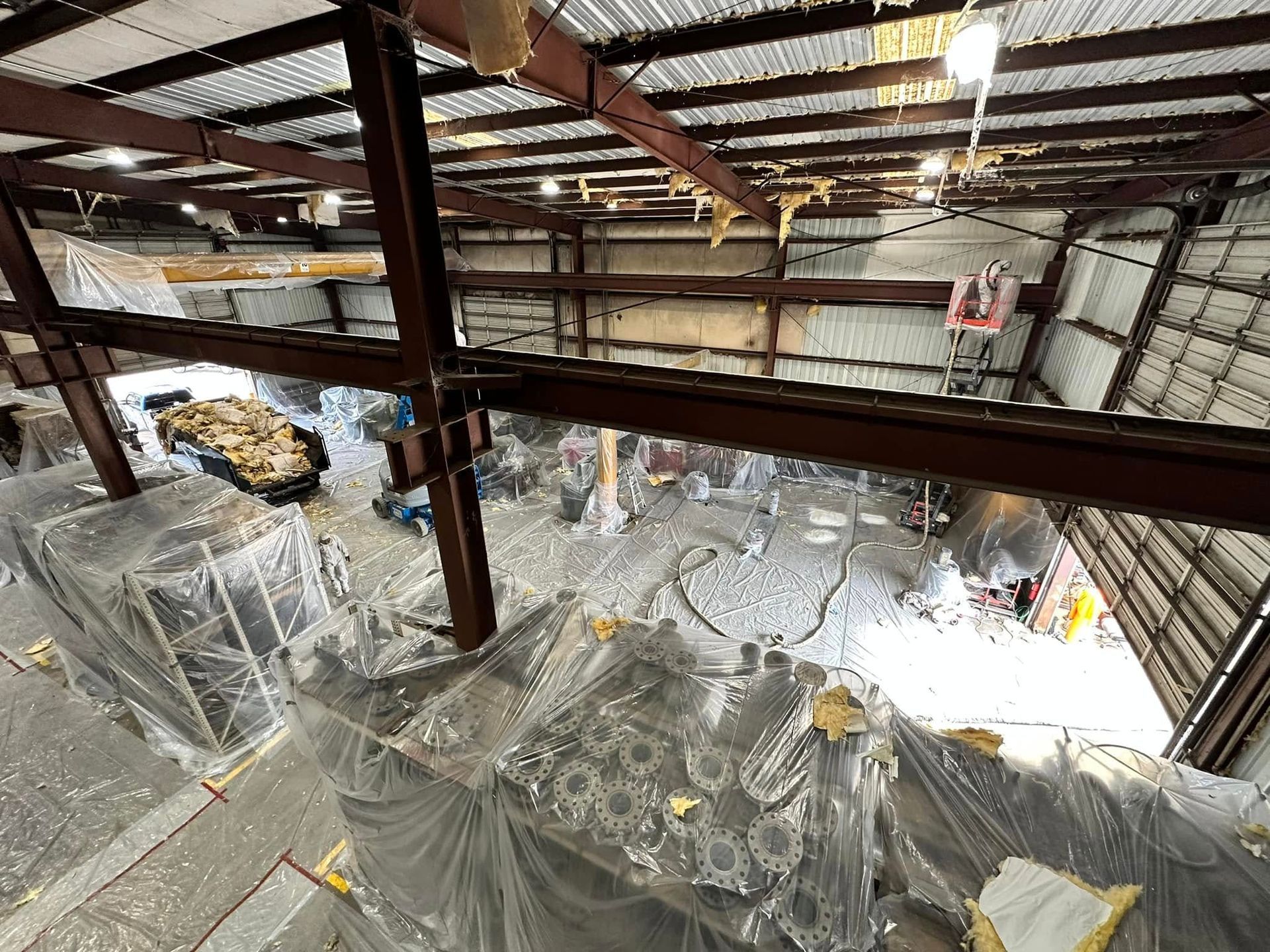 Warehouse interior with steel beams and equipment covered in plastic. Overhead view.