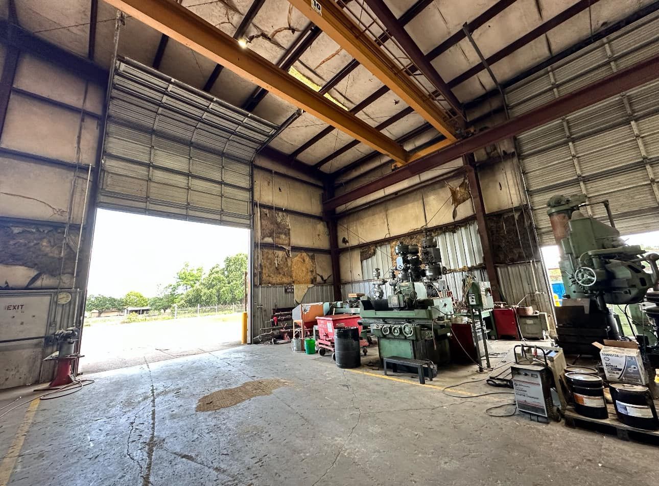 Interior of a warehouse with open bay door. Machinery and equipment fill the space.