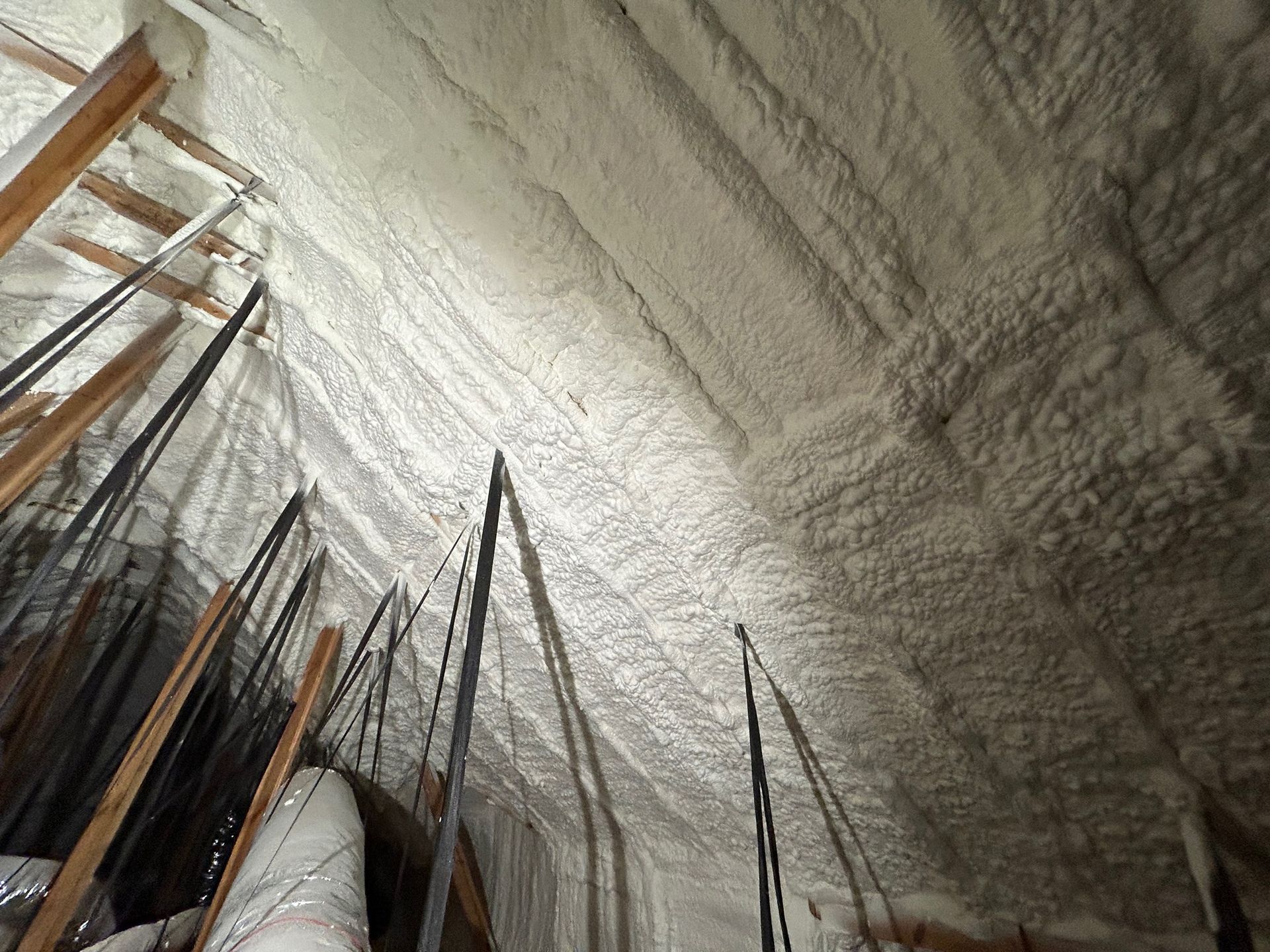 Spray foam insulation in attic, covering rafters and ceiling; interior view.