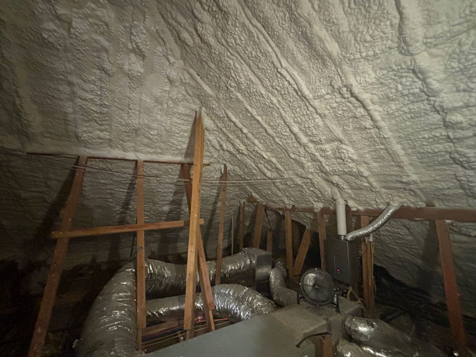 Attic interior with spray foam insulation on the roof and ductwork below.