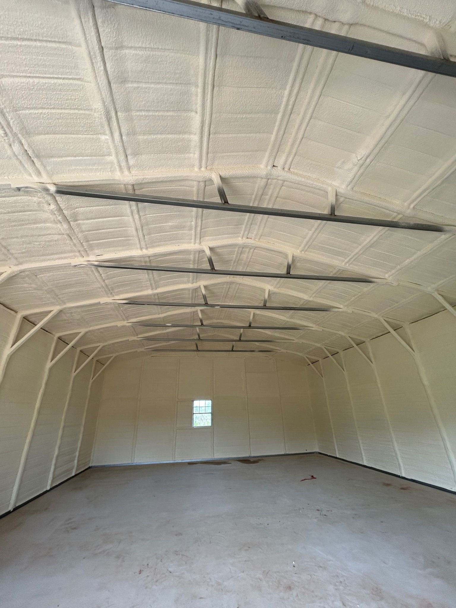 Interior of a building with foam insulation on the walls and ceiling. The space is empty with a concrete floor.