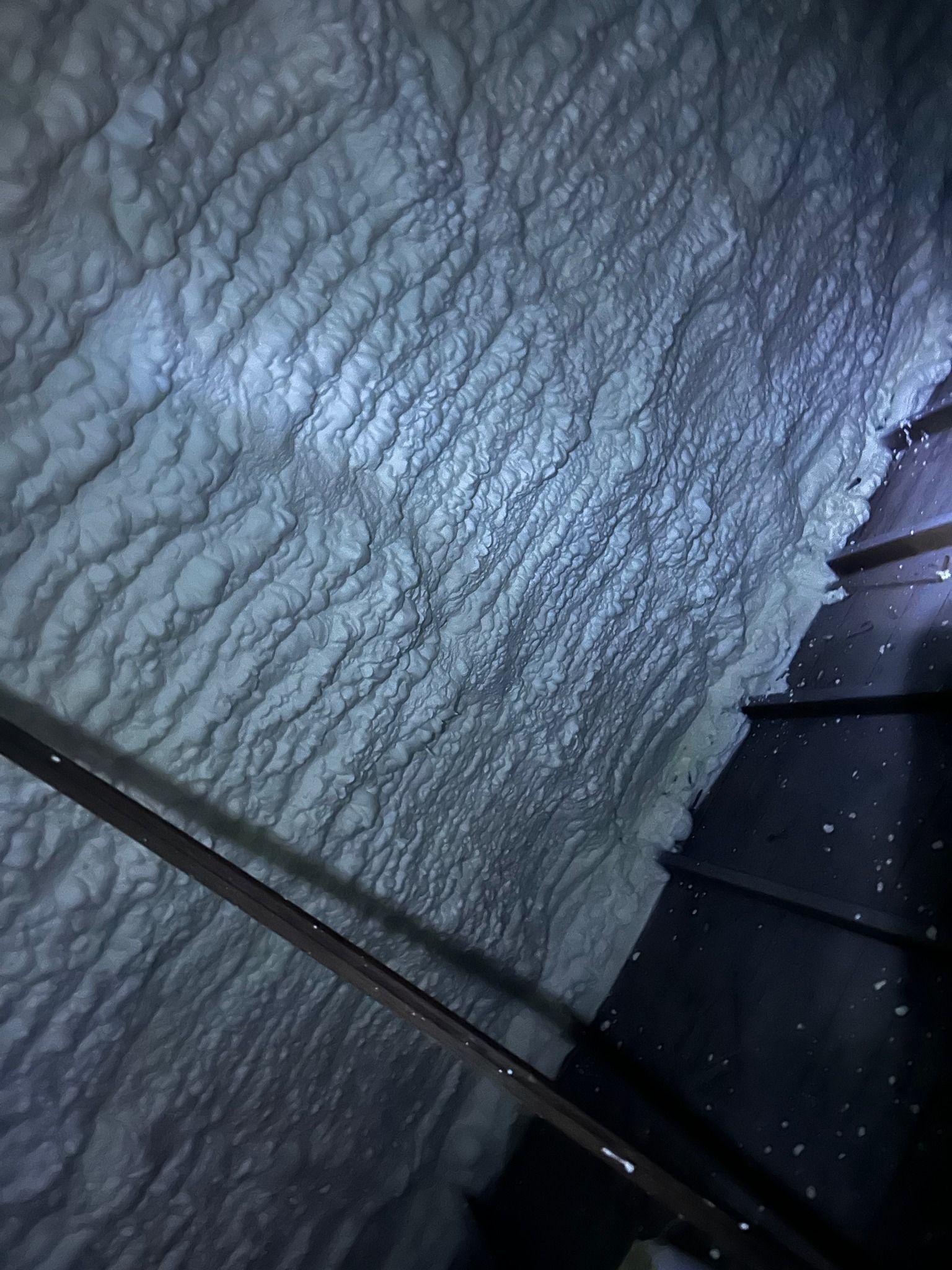 Spray foam insulation on a slanted wall, next to a dark staircase.
