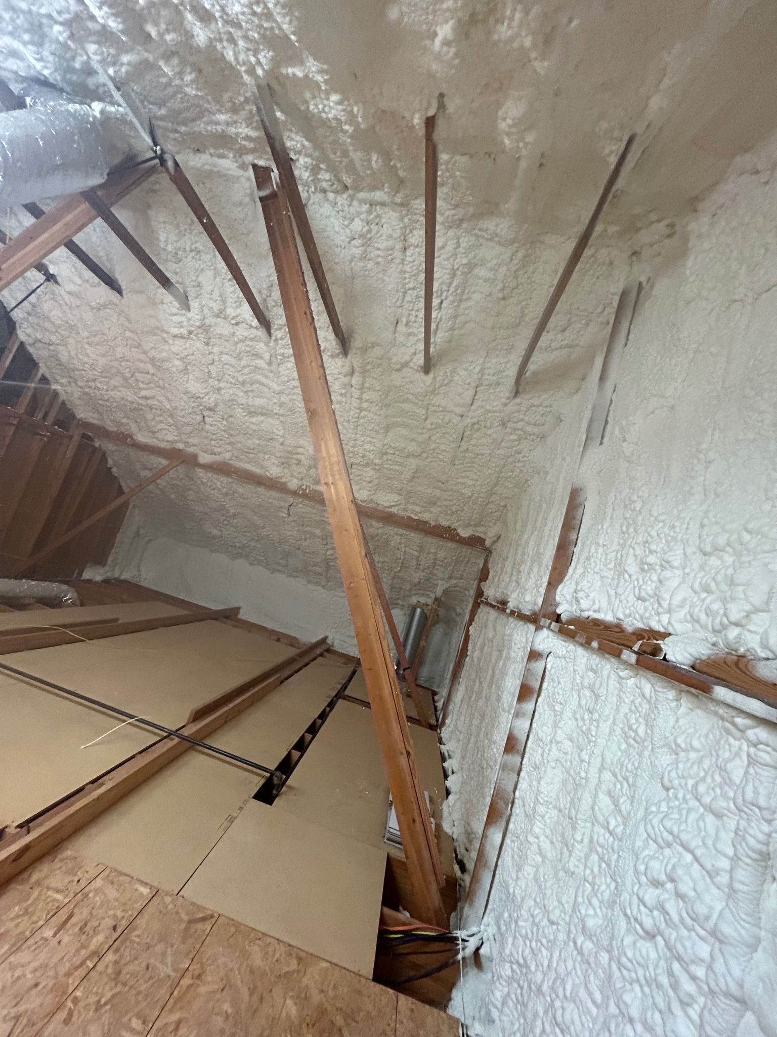 Attic space with spray foam insulation on the roof and walls, wooden supports visible.
