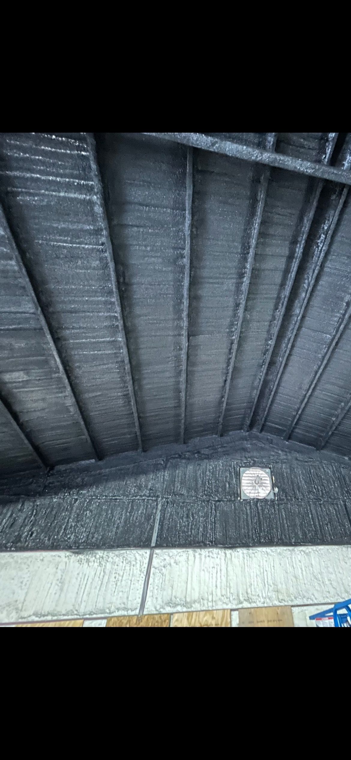 View of a dark, corrugated ceiling with supporting beams, and a dark substance piled below.