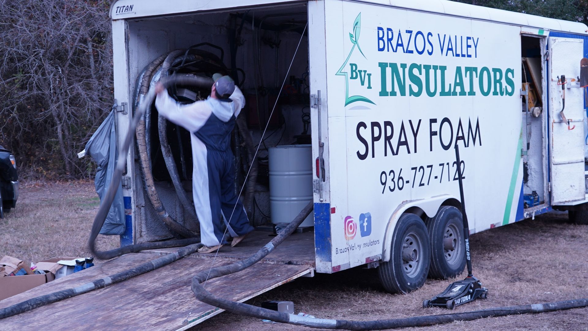Man in protective suit handling hoses near spray foam trailer.
